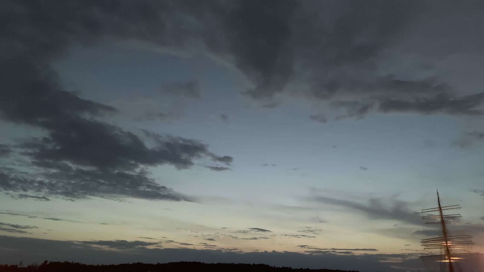 A tall ship's rigging silhouetted against a cloudy dusk sky.