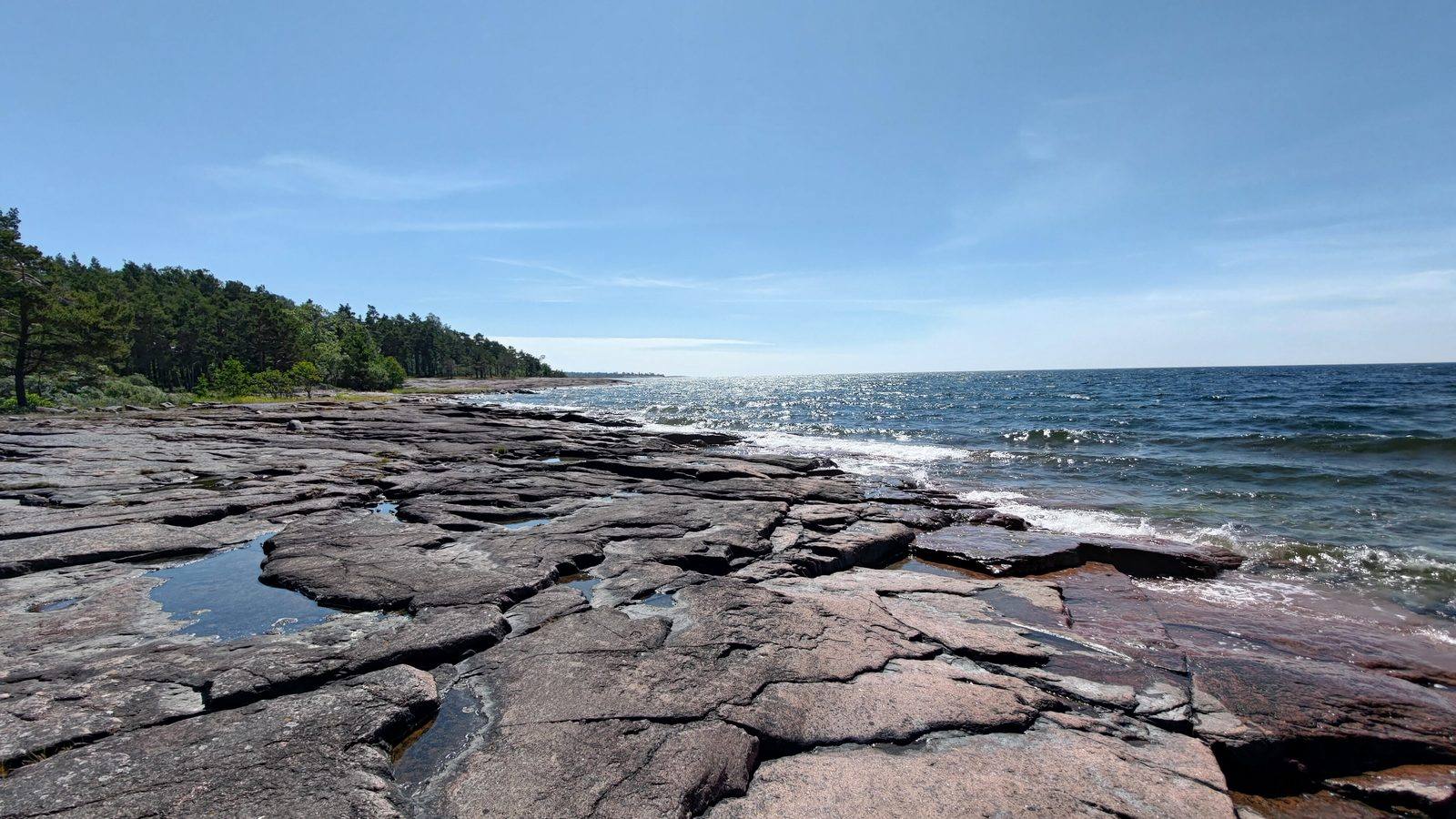 A flat, cracked rock shelf leading into the sea under a clear blue sky.